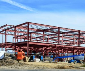 Commercial construction site showing Steel I beams and steel framing for a new commercial building with equipment in the foreground and sky in the background.